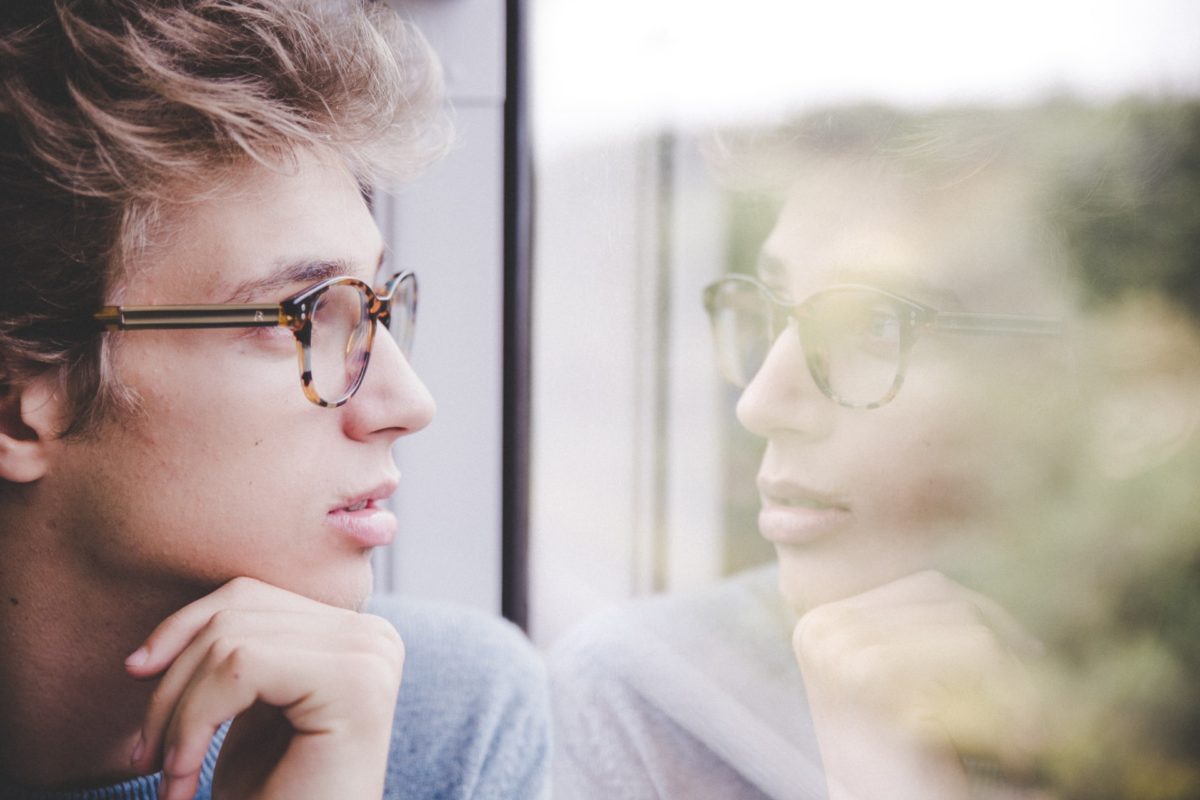 person wearing glasses looking at reflection in window