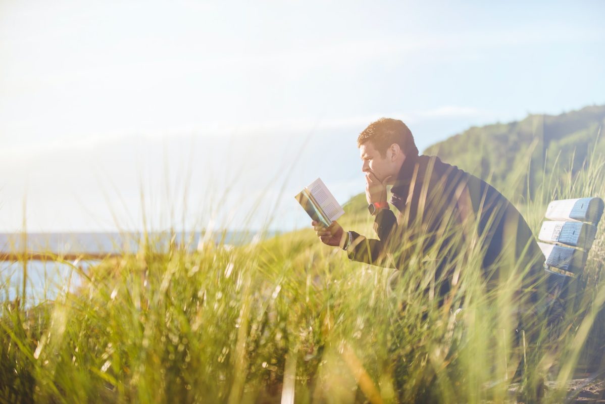 man reading book near lake during the day